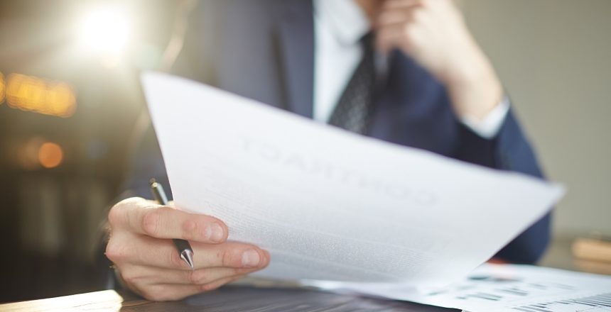 Closeup portrait of unrecognizable successful businessman wearing black formal suit analyzing documents and finance statistics at desk, thinking