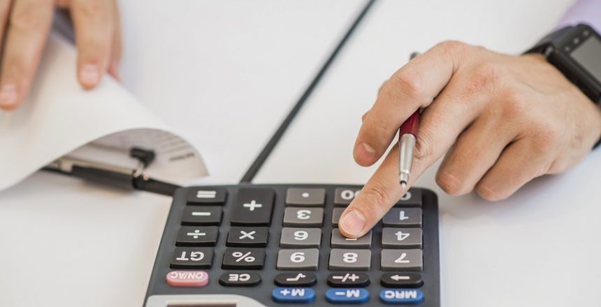 Close-up Of Businessman Calculating Invoices Using Calculator