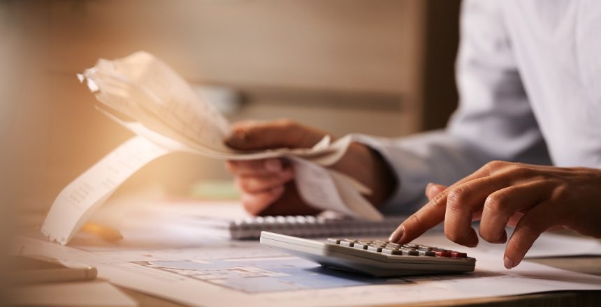 Close-up of economist using calculator while going through bills and taxes in the office.