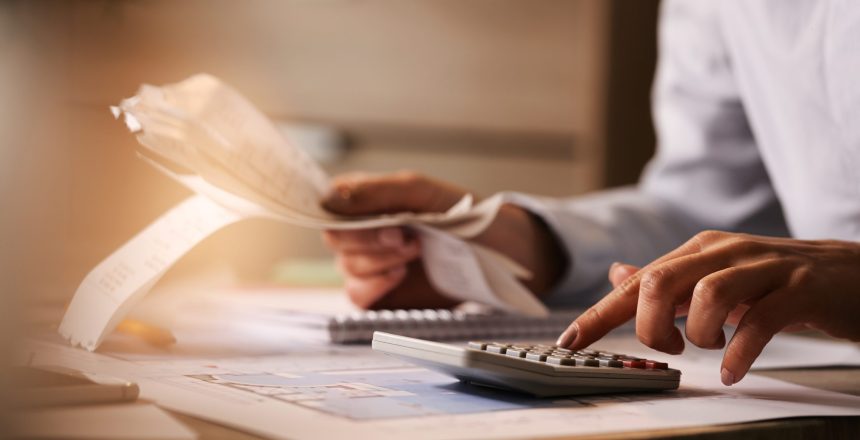 Close-up of economist using calculator while going through bills and taxes in the office.