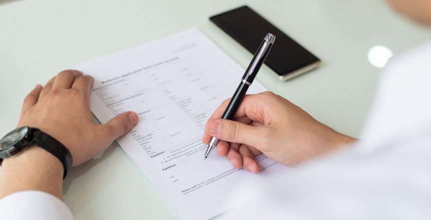 Hands of businessman or student filling application form. Close-up of young Caucasian man sitting at table and signing document. Job search concept
