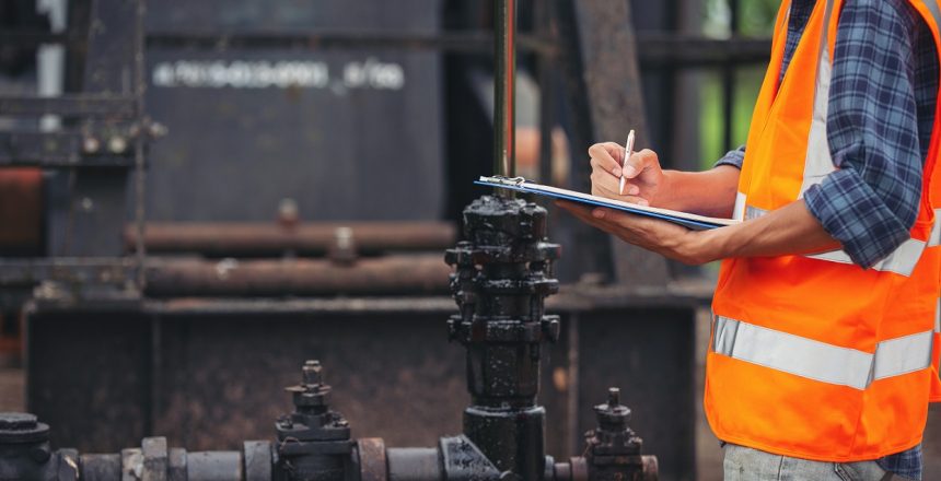 Workers standing and checking beside working oil pumps.
